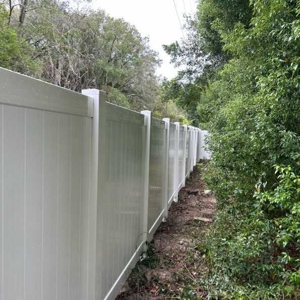 White vinyl privacy fence along a wooded path